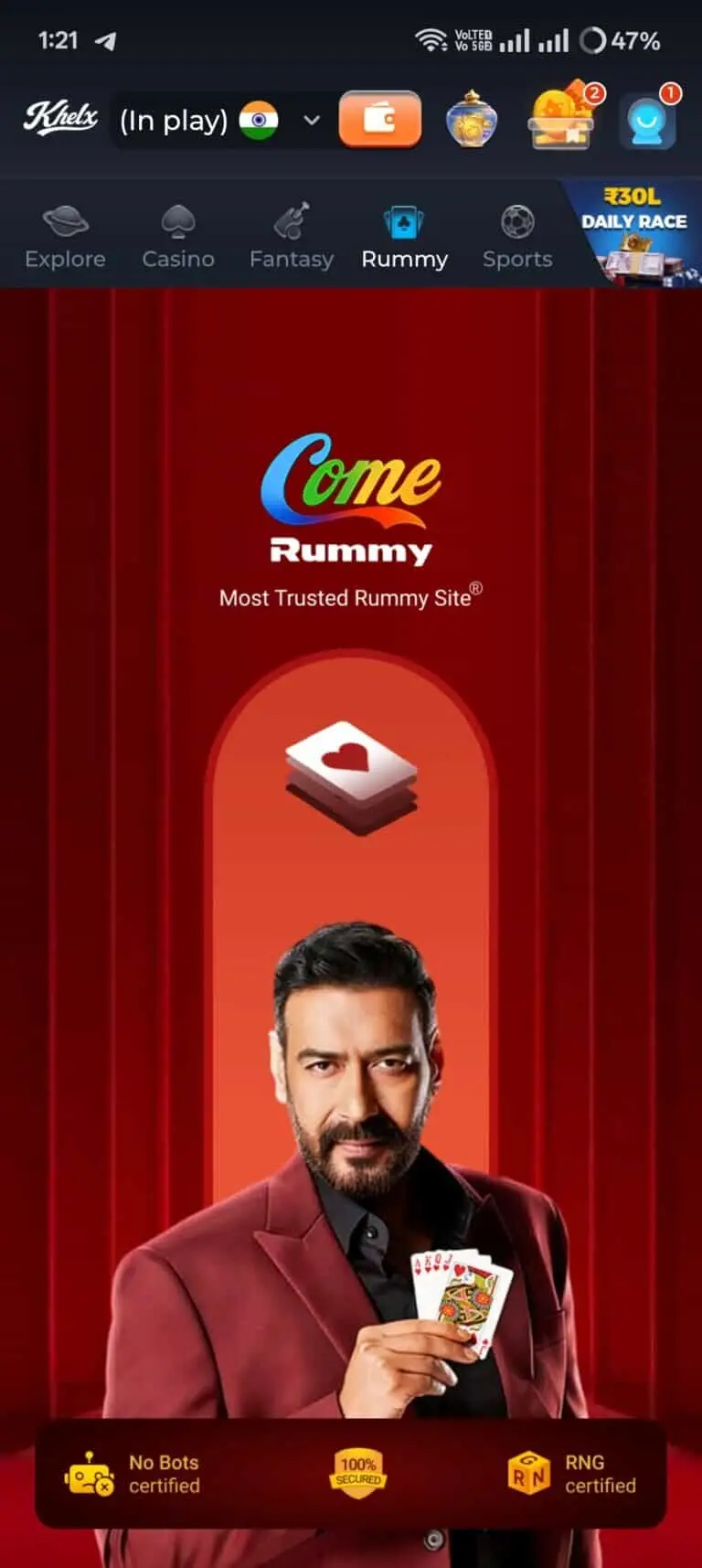 Khelx Game app interface showing the Rummy section, featuring actor Ajay Devgn holding playing cards. The screen displays the Come Rummy logo, the 'Most Trusted Rummy Site' tagline, and trust badges for 'No Bots certified', '100% Secured', and 'RNG certified'. The top navigation bar highlights the Rummy tab.